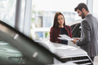 © Martin Barraud/Caia Image - Car saleswoman showing brochure to male customer in car dealership showroom