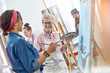 © Agnieszka Olek/Caia Image - Smiling female artists paintbrushes palettes painting in art class studio