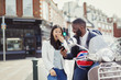 © Caiaimage/Paul Bradbury/Caia Image - Young couple laughing, using cell phone at motor scooter on sunny urban street