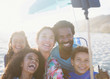 © Sam Edwards/Caia Image - Happy, playful multi-ethnic family taking selfie selfie stick on sunny summer beach