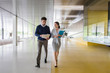 © Caiaimage/Martin Barraud/Caia Image - Businessman businesswoman walking discussing paperwork in modern office corridor