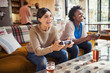 © Caiaimage/Paul Bradbury/Caia Image - Laughing women friends playing video game on living room sofa