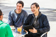 © David Mitchell/Caia Image - Male friends with digital tablet laughing at sidewalk cafe