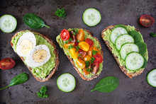 Healthy Avocado Toast Assortment. Eggs, Tomatoes And Cucumber Spinach. Flat Lay Over A Dark Background.