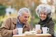 © Tom Merton/Caia Image - Senior couple with smart phone, eating lunch and drinking coffee in park