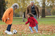 © Tom Merton/Caia Image - Grandparents playing soccer with granddaughter in autumn park