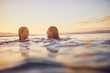 © Trevor Adeline/Caia Image - Young couple swimming in ocean at sunset