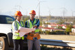 © Trevor Adeline/Caia Image - Engineers reviewing blueprints near wind turbine farm