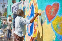 Senior Man Painting Mural On Sunny Urban Wall