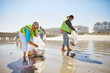 © Trevor Adeline/Caia Image - Female volunteers picking up litter on sunny wet sand beach