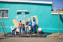 Community Volunteers Painting Vibrant Mural On Sunny Urban Wall