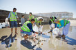 © Trevor Adeline/Caia Image - Volunteers cleaning up litter on sunny, wet sand beach