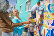 © Trevor Adeline/Caia Image - Community volunteers painting vibrant mural on sunny urban wall