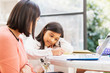 © Tom Merton/Caia Image - Mother at laptop watching daughter doing homework at table
