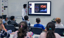 Male Teacher Leading Lesson At Touch Screen Television In Classroom