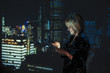 © Paul Bradbury/Caia Image - Double exposure businesswoman using digital tablet against highrise lights at night