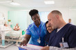 © Tom Merton/Caia Image - Doctors and nurse making rounds, discussing medical chart in hospital ward
