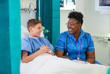 Female Nurse Talking With Boy Patient In Hospital Room