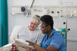 © Tom Merton/Caia Image - Female nurse discussing paperwork with senior patient in hospital room