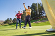 © Trevor Adeline/Caia Image - Happy male golfers cheering on sunny putting green