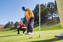 Male Golfer Putting At Hole On Sunny Golf Course Putting Green