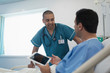 © Sam Edwards/Caia Image - Male nurse talking with patient using digital tablet in hospital bed