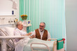 © Tom Merton/Caia Image - Senior man visiting wife resting in hospital room