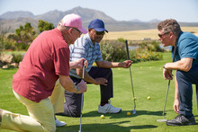 Male Golfers Kneeling And Talking On Sunny Practice Putting Green