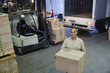 © Ryan Lees/Caia Image - Portrait smiling worker carrying cardboard box at distribution warehouse loading dock