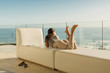 © Tom Merton/Caia Image - Woman on luxury balcony relaxing laying on bench looking at sunny ocean view