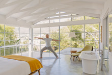 Mature Man Practicing Yoga Warrior 2 Pose In Luxury Bedroom
