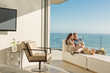 © Tom Merton/Caia Image - Couple using digital tablet on chaise lounge on sunny luxury balcony with ocean view