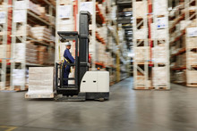 Worker Operating Forklift Moving Pallet Of Boxes In Distribution Warehouse