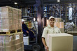 © Ryan Lees/Caia Image - Portrait smiling worker carrying cardboard box at distribution warehouse loading dock