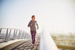 © Ryan Lees/Caia Image - Female runner running on sunny urban footbridge at sunrise