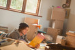© Justin Pumfrey/Caia Image - Young man reading book surrounded by moving boxes in apartment