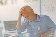 © Tom Merton/Caia Image - Tired, stressed male doctor with head in hands in doctor‚Äôs office