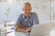 © Tom Merton/Caia Image - Smiling male doctor working at laptop in doctor‚Äôs office