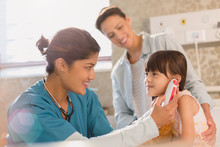 Female Nurse Using Digital Thermometer In Ear Of Girl Patient In Examination Room