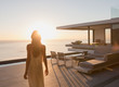 © Tom Merton/Caia Image - Woman walking on tranquil sunset modern, luxury home showcase exterior patio with ocean view