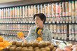 © Tom Merton/Caia Image - Young woman with headphones grocery shopping, holding orange in market