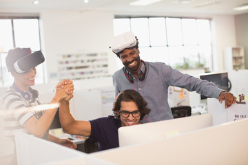 Smiling, enthusiastic computer programmers high-fiving, testing virtual reality simulator glasses