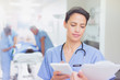 © Tom Merton/Caia Image - Female surgeon with digital tablet reviewing clipboard paperwork in hospital corridor