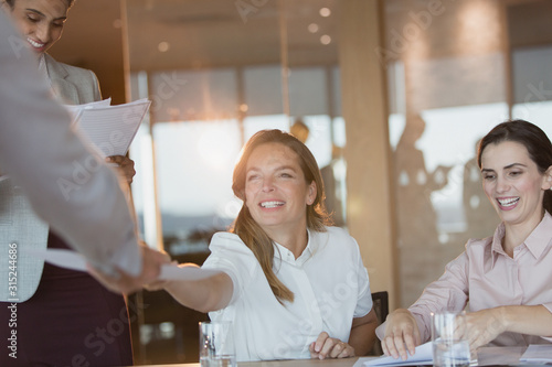 Fototapeta Smiling businesswoman handing paperwork to colleague in conference room meeting