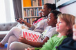 © Paul Bradbury/Caia Image - Family and friends watching movie and eating popcorn on living room sofa