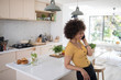 © Sam Edwards/Caia Image - Smiling young woman talking on smart phone in kitchen