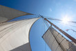 © Martin Barraud/Caia Image - Sailboat sails blowing in wind below sunny blue sky