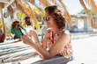 © Paul Bradbury/Caia Image - Carefree woman drinking cocktail and using smart phone at sunny beach bar