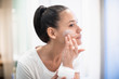 © Sam Edwards/Caia Image - Woman applying moisturizer to face in bathroom mirror
