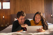 © Tom Merton/Caia Image - Happy young couple with headphones sharing digital tablet on bed